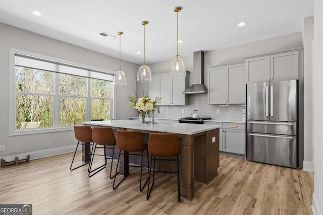 kitchen with a center island with sink, wall chimney exhaust hood, appliances with stainless steel finishes, light countertops, and backsplash