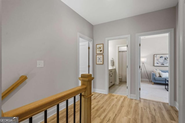 hall featuring light wood-type flooring, an upstairs landing, and baseboards