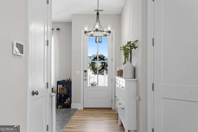 doorway to outside featuring light wood finished floors and a chandelier