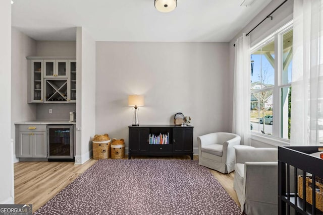 living area featuring a bar, light wood-style floors, beverage cooler, and baseboards