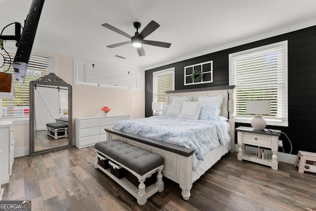 bedroom with a barn door, multiple windows, visible vents, and wood finished floors