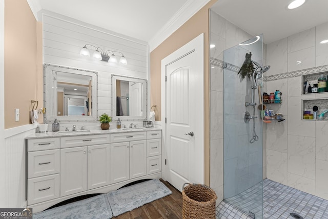 bathroom with double vanity, crown molding, a tile shower, and a sink