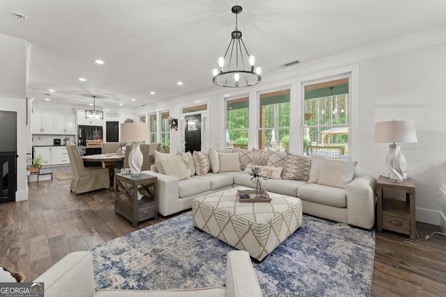 living room with crown molding, visible vents, dark wood-type flooring, and a notable chandelier