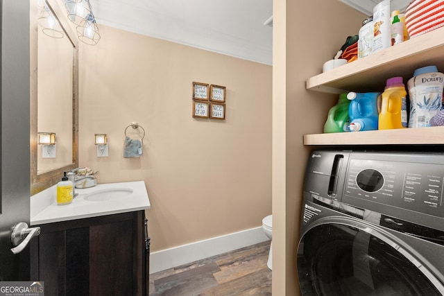 washroom featuring wood finished floors, a sink, baseboards, washer / dryer, and crown molding