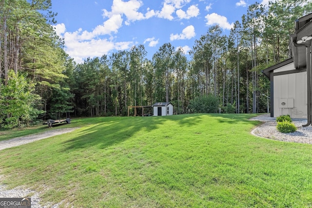 view of yard featuring an outbuilding, a forest view, and a storage shed