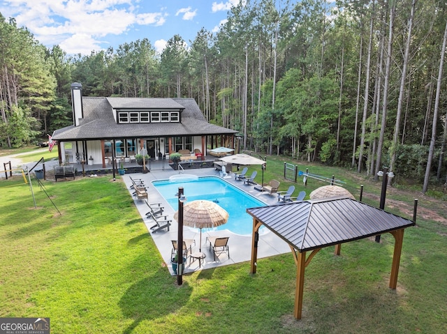 pool with a forest view, a lawn, a patio area, and fence