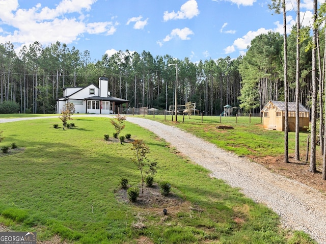 view of community featuring gravel driveway, a yard, volleyball court, a wooded view, and an outdoor structure