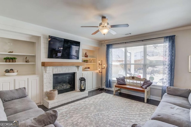 living area with wood finished floors, visible vents, baseboards, built in features, and a glass covered fireplace