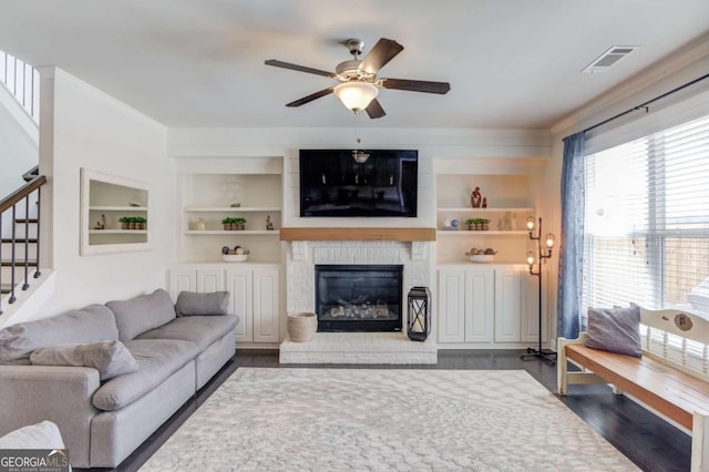 living area featuring ceiling fan, built in shelves, a fireplace, visible vents, and stairway