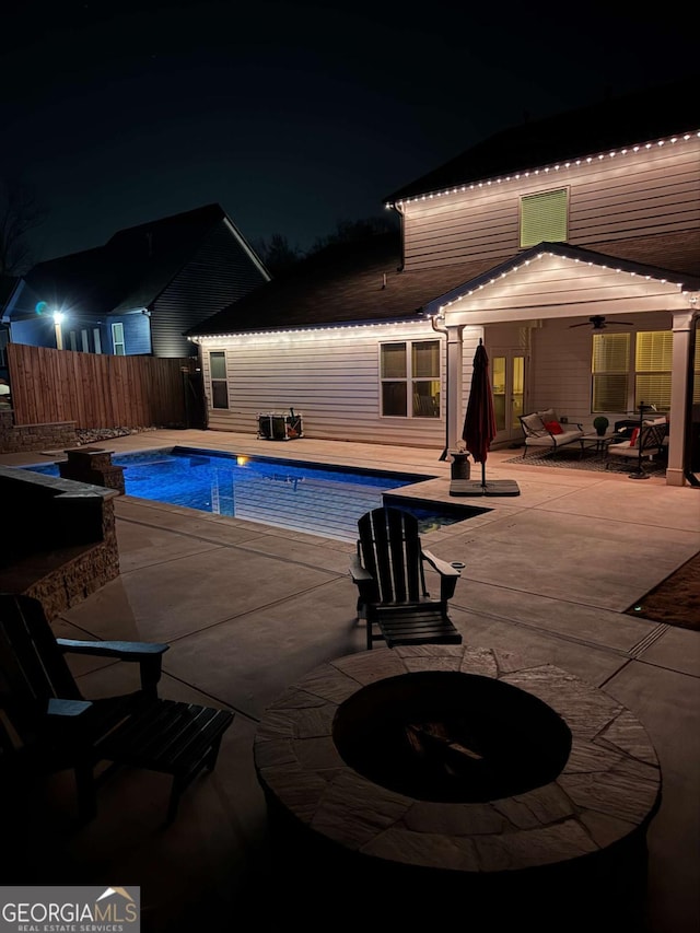 pool at night featuring a fenced in pool, fence, ceiling fan, and a patio