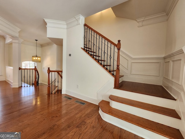 stairway featuring ornamental molding, wood finished floors, visible vents, and a decorative wall