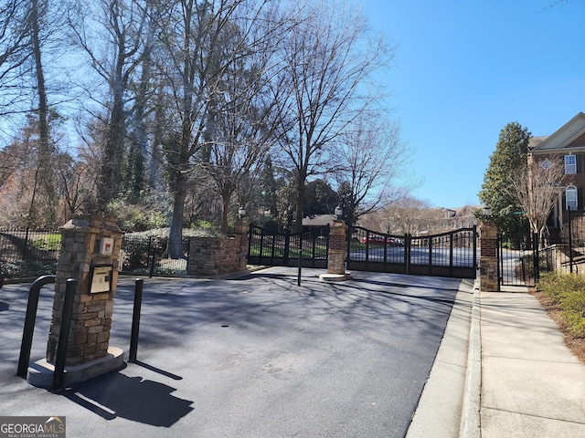 view of road featuring a gate, sidewalks, curbs, and a gated entry