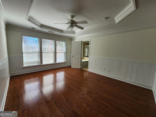 spare room with visible vents, a raised ceiling, a ceiling fan, wainscoting, and wood-type flooring