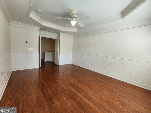 empty room featuring crown molding, a raised ceiling, wainscoting, ceiling fan, and wood finished floors