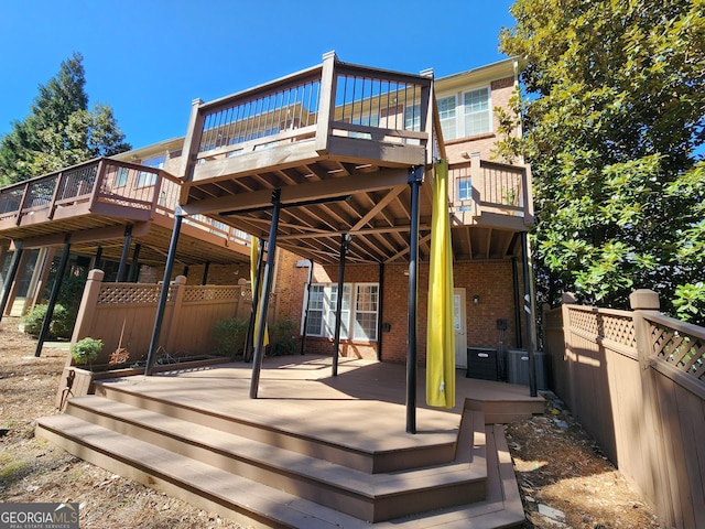 rear view of property with a deck, brick siding, and fence