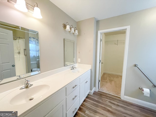 full bath featuring double vanity, a walk in closet, a sink, and wood finished floors