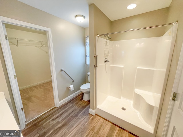 bathroom with wood finished floors, walk in shower, toilet, and baseboards