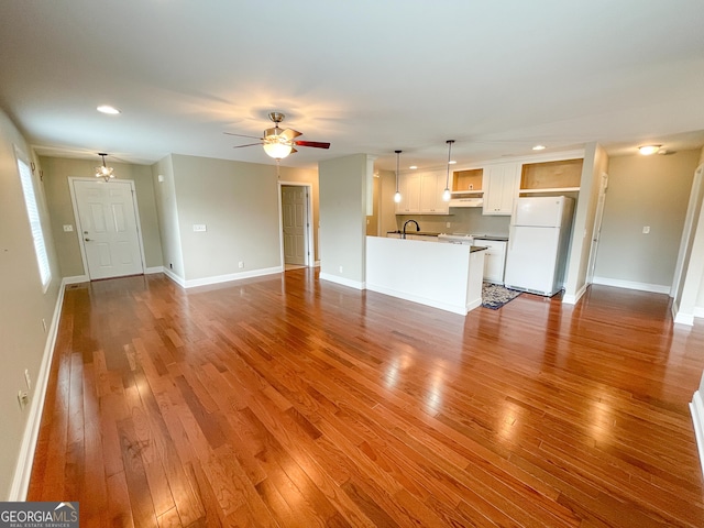 unfurnished living room with ceiling fan with notable chandelier, wood-type flooring, a sink, and baseboards