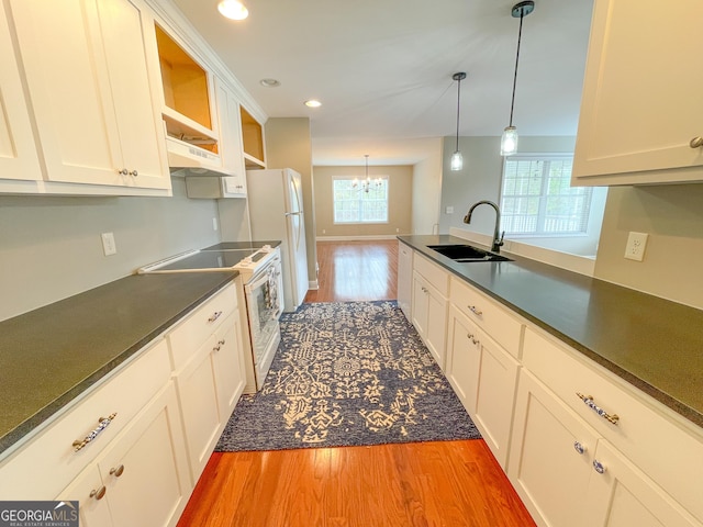 kitchen with light wood-type flooring, white appliances, dark countertops, and a sink