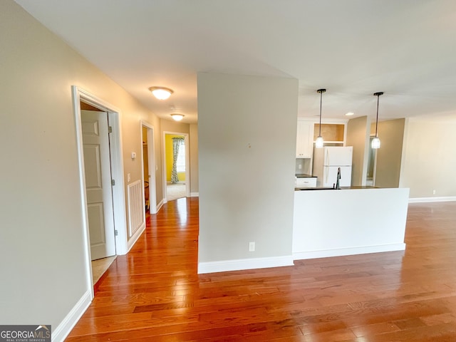 kitchen with white cabinetry, baseboards, light wood-type flooring, freestanding refrigerator, and decorative light fixtures