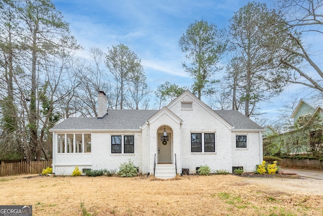 view of front of home featuring a shingled roof, brick siding, fence, and a chimney