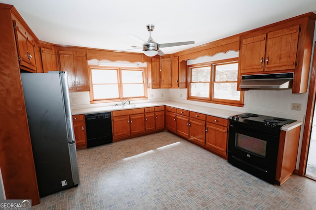 kitchen with brown cabinetry, under cabinet range hood, light countertops, black appliances, and backsplash