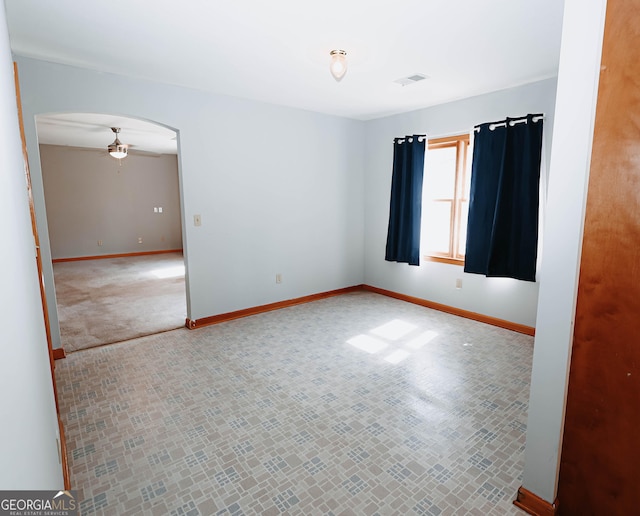 carpeted empty room featuring baseboards, visible vents, arched walkways, and a ceiling fan