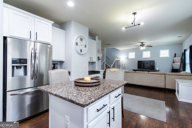 kitchen with dark wood-style floors, a center island, white cabinetry, dark stone counters, and stainless steel fridge