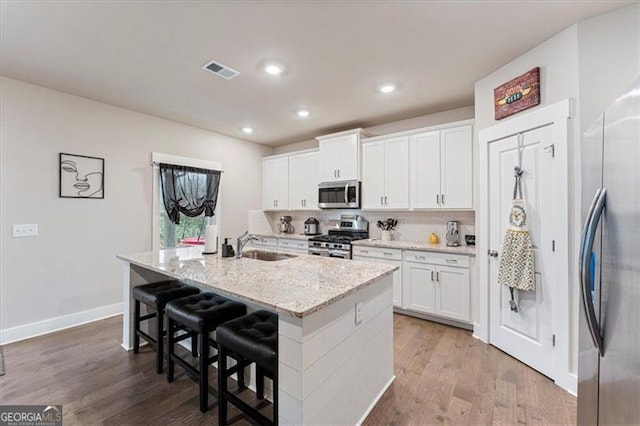 kitchen featuring stainless steel appliances, wood finished floors, visible vents, white cabinetry, and a center island with sink