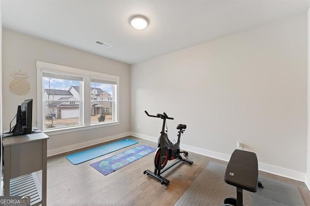 exercise room with wood finished floors, visible vents, and baseboards