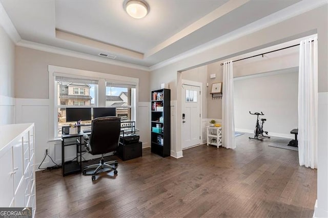 office featuring a decorative wall, wood finished floors, visible vents, wainscoting, and a tray ceiling