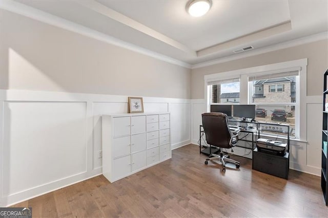 office area with visible vents, a raised ceiling, wood finished floors, and a decorative wall