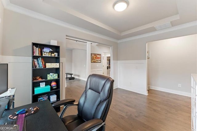 home office featuring a raised ceiling, a wainscoted wall, visible vents, and wood finished floors