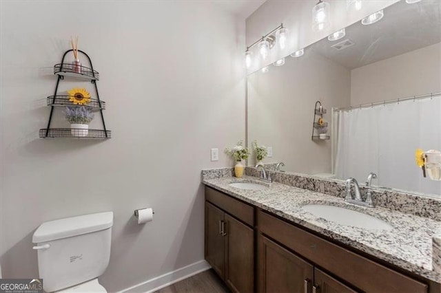 bathroom with baseboards, a sink, toilet, and double vanity