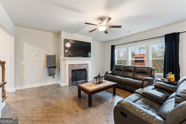 living area with a stone fireplace, wood finished floors, a ceiling fan, baseboards, and stairway