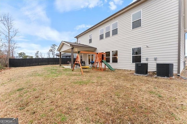 rear view of house featuring a playground, fence, central AC, and a yard