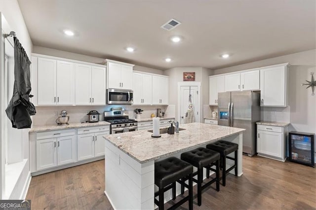 kitchen featuring stainless steel appliances, visible vents, a kitchen island with sink, white cabinets, and wood finished floors