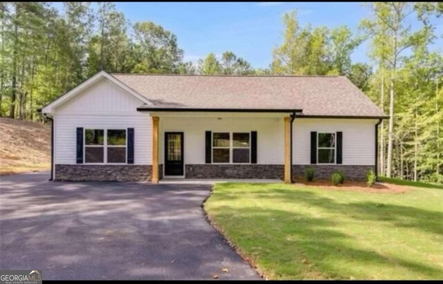 view of front of property featuring aphalt driveway, a front yard, and stone siding