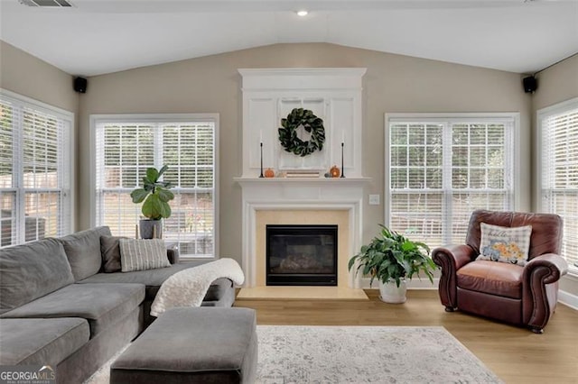 living area with lofted ceiling, light wood finished floors, a fireplace, and visible vents