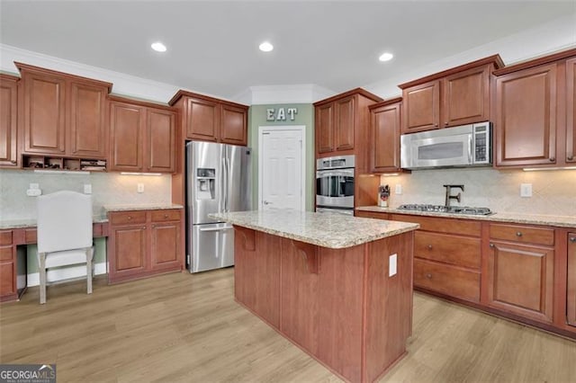 kitchen with light wood finished floors, a kitchen island, ornamental molding, and stainless steel appliances