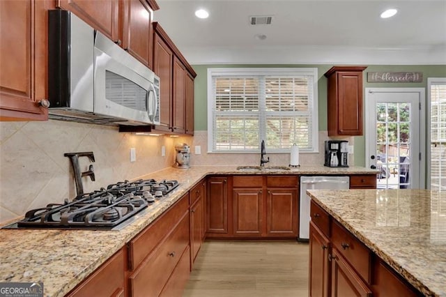 kitchen with visible vents, appliances with stainless steel finishes, light stone countertops, crown molding, and a sink