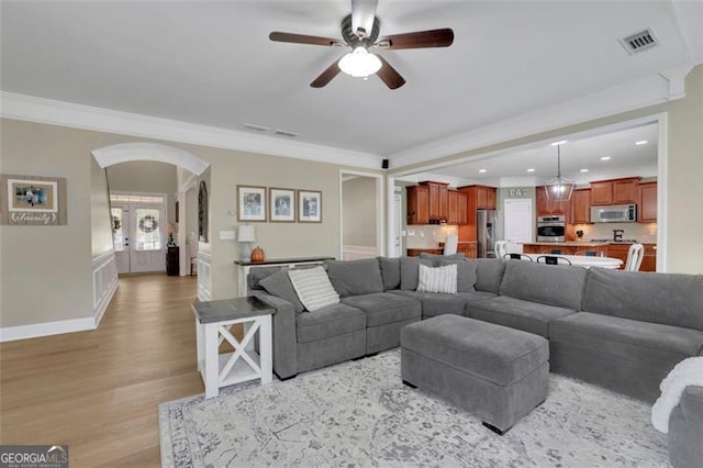 living room featuring arched walkways, ornamental molding, light wood-type flooring, and visible vents