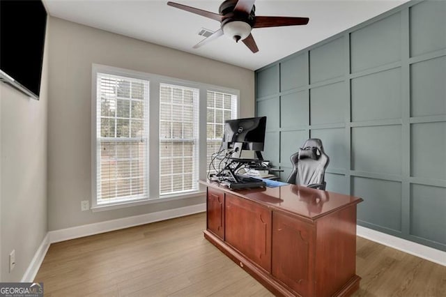 office featuring visible vents, baseboards, ceiling fan, light wood-style floors, and a decorative wall