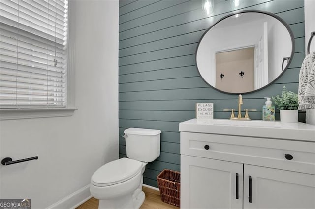 half bathroom featuring baseboards, vanity, toilet, and wood finished floors