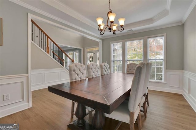 dining room featuring wood finished floors, stairs, ornamental molding, a tray ceiling, and an inviting chandelier