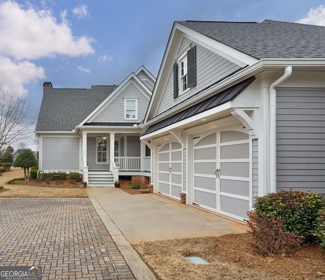 view of front of house with metal roof, covered porch, a garage, a shingled roof, and concrete driveway