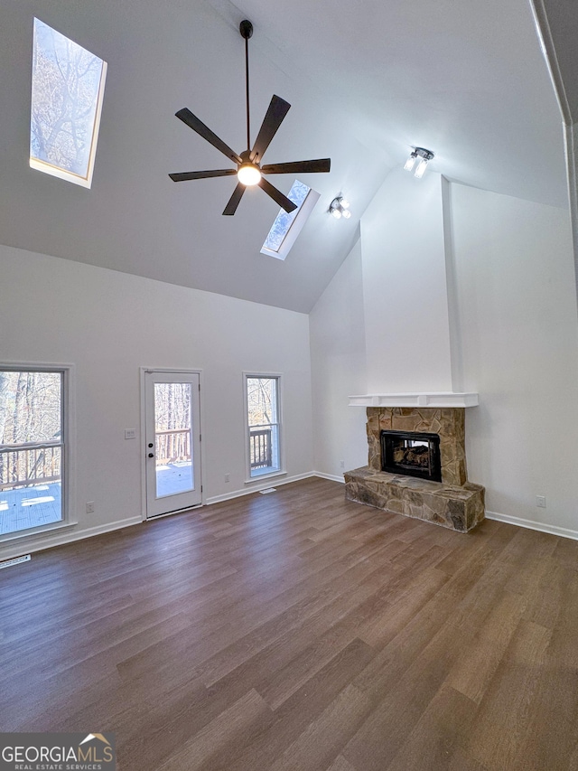 unfurnished living room featuring dark wood-type flooring, ceiling fan, a fireplace, a skylight, and high vaulted ceiling