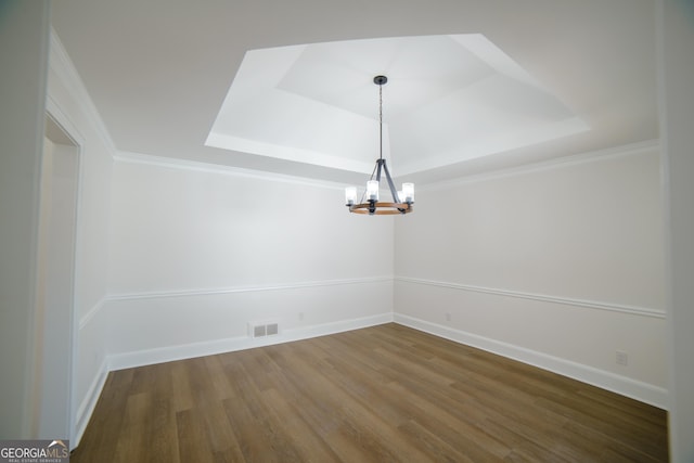 spare room with visible vents, a raised ceiling, wood finished floors, baseboards, and a chandelier