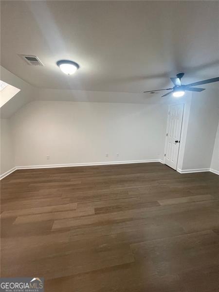 additional living space featuring a ceiling fan, visible vents, vaulted ceiling, and dark wood-style flooring