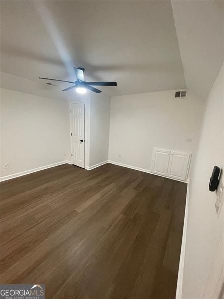 empty room with a ceiling fan, baseboards, visible vents, and dark wood-type flooring